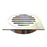 Square stainless steel shower drain grate with circular slotted bars, modern chrome finish on wood floor.