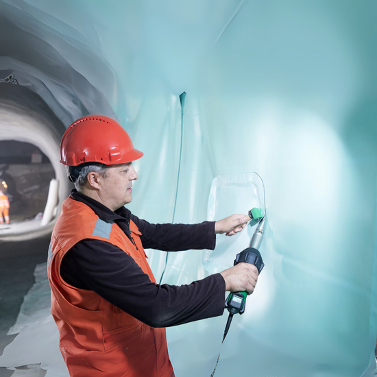 Worker using handheld hot air welder to seam blue geomembrane liner in tunnel construction
