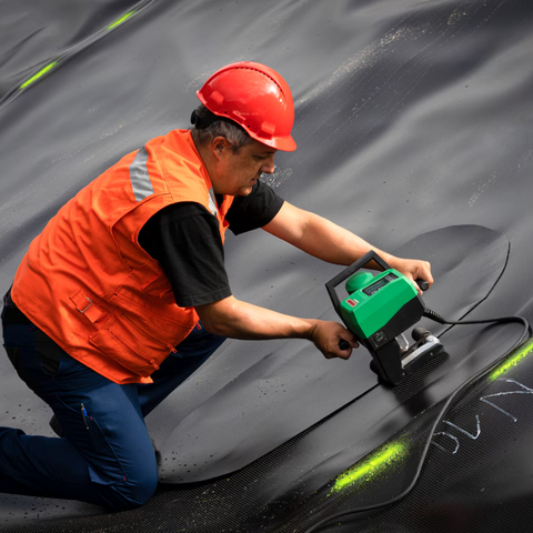 Roofer using green corded chalk line tool to mark fluorescent lines on black EPDM flat roof, hi-vis vest, hard hat