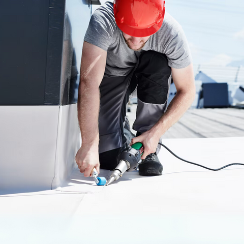 Roofer welds waterproofing membrane seams on flat roof using Leister Triac AT heat gun for precise thermoplastic bonds.