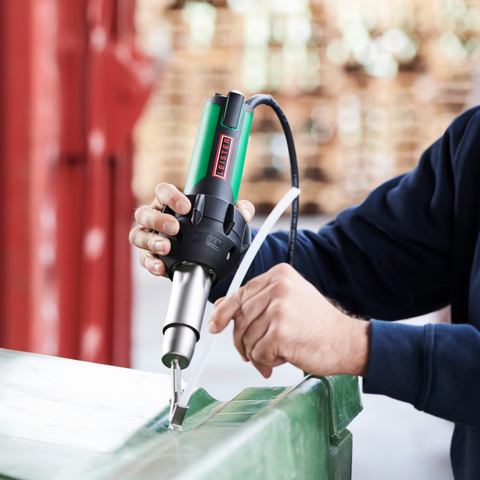 Steinel green professional heat gun in use, hot air nozzle on metal edge, industrial workshop
