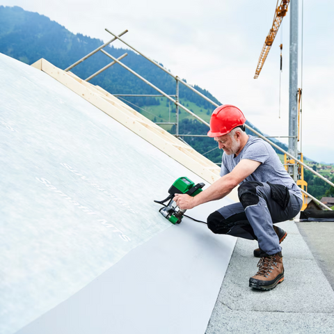 Cordless jigsaw cutting roof insulation board – worker in red hard hat on alpine construction site
